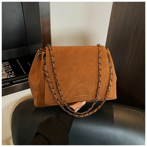 Close-up of retro brown suede tote bag with black metal chain strap on a wooden stand