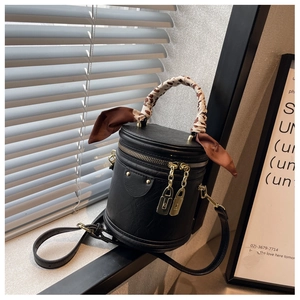 Detail of black cylinder bucket bag with silk scarf handle and golden zipper hardware
