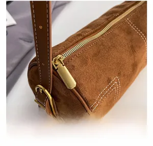 Detail showing smooth gold zipper and contrast stitching on brown suede cylinder bag