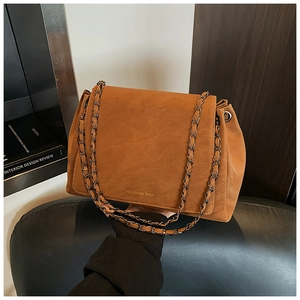 Macro detail of brown suede chain bag featuring silver logo and metallic shoulder strap