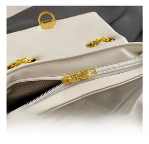 Close-up of white quilted crossbody bag showing golden metal zipper and texture details