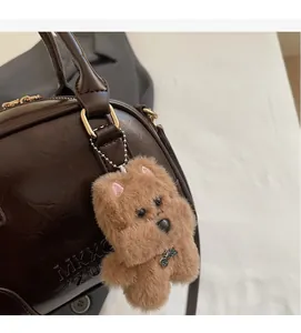 Detail of dark brown leather handbag with MKXC logo and plush dog charm with metal chain