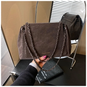 Detailed shot of dark brown suede shoulder bag featuring a gold chain strap and logo