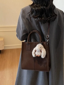 Brown leather tote bag with bunny charm shown on model in minimalist interior