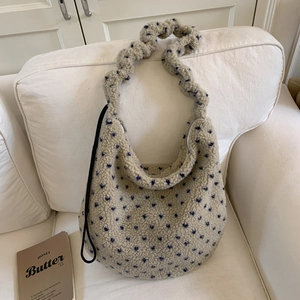 Detail of fuzzy tote bag with blue heart patterns and ruched strap on a white sofa