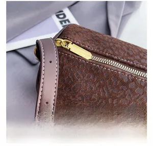 Detailed view of matte leopard print cylindrical bag with gold zipper and leather strap
