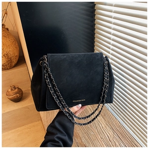 Close-up of matte black leather chain bag with gold logo and woven metal strap
