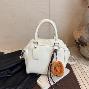 Detail der cremeweißen Handtasche aus Leder mit Plüsch-Brezel-Anhänger auf dunklem Grund