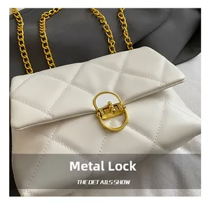 Close-up of golden metal lock and quilted leather pattern on a white chain bag