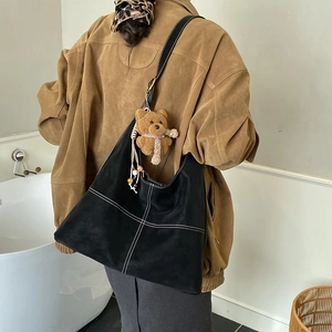 Dettaglio borsa shopper nera con cuciture a contrasto e ciondolo orsetto di peluche