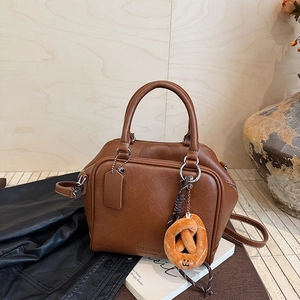 Detail der karamellfarbenen Handtasche mit Plüsch-Schmetterlingsanhänger und Logo