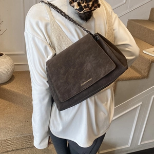 Detail of dark brown suede crossbody bag showing metal chain strap and golden logo
