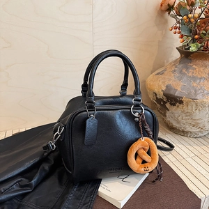 Detail der schwarzen Leder-Bowlingtasche mit Vintage-Textur und Brezel-Anhänger