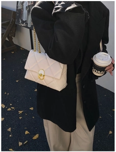 Detail of white quilted handbag with golden chain strap and circular metal turn-lock clasp