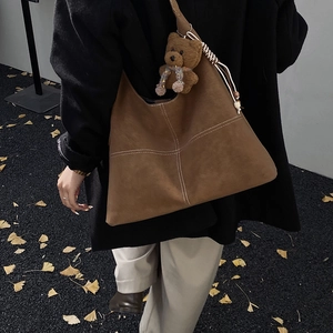 Dettaglio della borsa tote in pelle scamosciata marrone con cuciture bianche e orsetto