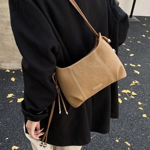 Detail of camel brown leather crossbody bag with side fringe tassel on a dark coat