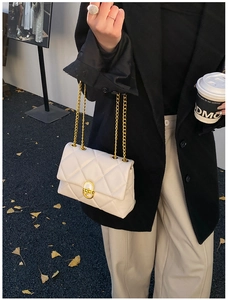 Close-up of white quilted leather bag with gold chain strap and rotary metal lock buckle