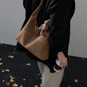 Dettaglio borsa tote in pelle scamosciata marrone con cuciture a contrasto e ciondolo orso
