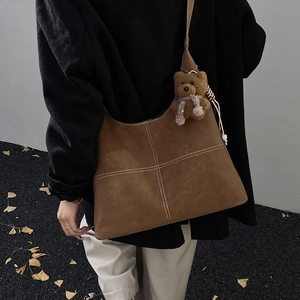 Dettaglio della borsa tote in pelle scamosciata marrone con cuciture e ciondolo orso
