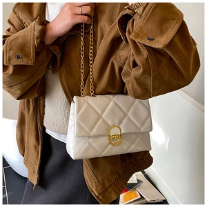 Detail of a quilted cream shoulder bag with gold chain strap on a stylish model