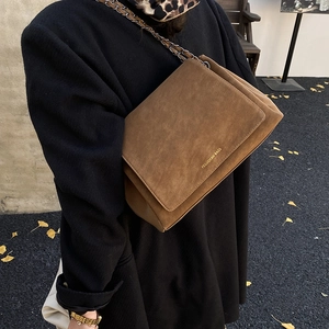 Detail of a brown suede chain bag with gold logo worn over a black winter coat