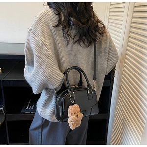 Detail of black Boston bag with teddy bear charm and adjustable shoulder strap on model