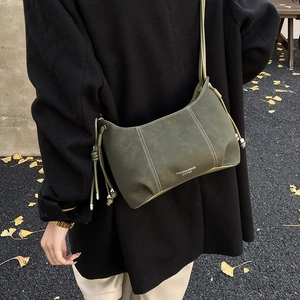 Detail of olive green leather crossbody bag with white stitching and drawstring beads