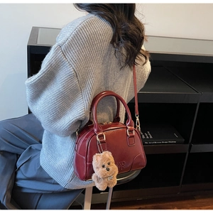 Detail of burgundy patent leather pillow bag with brown plush puppy charm on a gray sweater