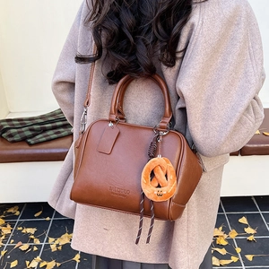 Braune Retro-Bowlingtasche im Detail mit Logo-Prägung und Plüsch-Brezel-Anhänger