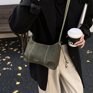 Detailed view of dark green leather shoulder bag with white stitching and metal ball charm