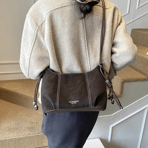 Close-up of dark brown leather shoulder bag with white stitching and metal bead detail