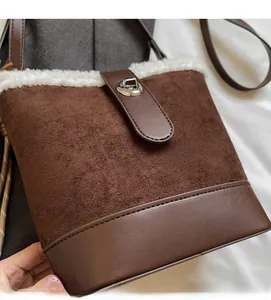 Detalle del bolso tipo cubo de ante marrón con ribete de pelo blanco y cierre giratorio