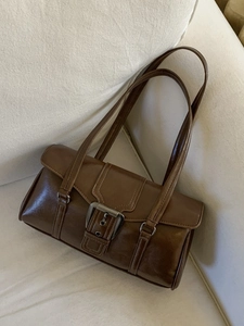Vintage brown waxed leather shoulder bag with bold metal buckles on a fabric sofa