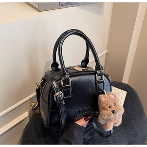 Detail of black pebbled leather bowling bag featuring MKXO logo and plush dog charm