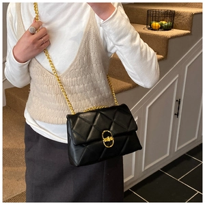 Detail of black quilted leather hobo bag with gold chain strap on a model indoors