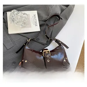 Détail du sac bandoulière en cuir verni bordeaux avec boucle dorée et rivets chic