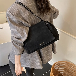 Detail of black suede chain bag showing gold lettering and woven shoulder strap