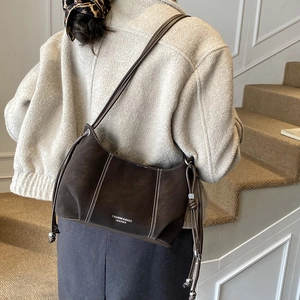 Detail of mocha brown leather crossbody bag with white stitching and drawstring design