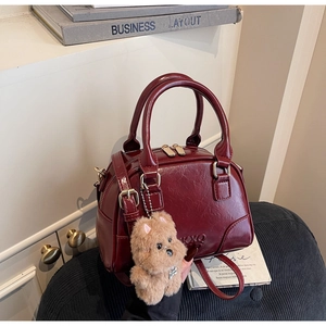 Detail of burgundy glossy leather pillow bag with plush bear charm and handle