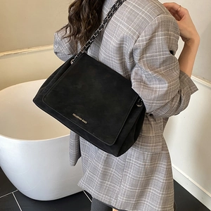 Black matte suede shoulder bag with gold chain strap detail on checkered blazer model