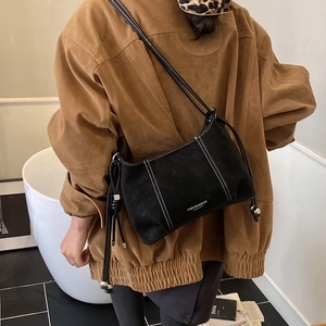 Detail of black suede shoulder bag with white contrast stitching and drawstring strap