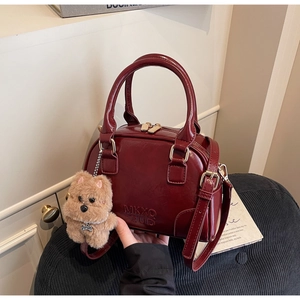 Detail of burgundy glossy handbag with MKXQ 2UD embossing and a brown teddy bear charm