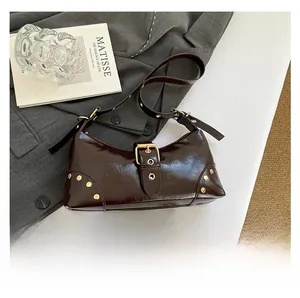 Détail d'un sac sous le bras en cuir marron avec clous dorés et bandoulière sur un magazine