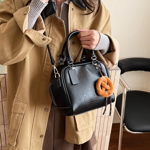 Nahaufnahme der schwarzen Bowling-Tasche mit Ledertextur und Plüsch-Brezel-Anhänger