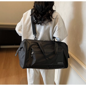 Gros plan du sac de voyage noir imperméable avec bandoulière et détail du logo métallique