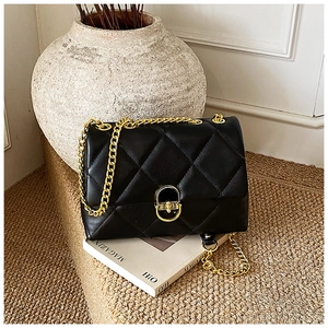 Close-up of black quilted PU leather shoulder bag with golden chain and oval turn-lock