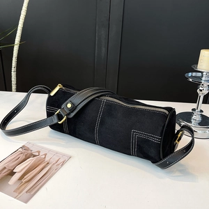 Detail of matte black cylinder bag with white contrast stitching and gold zipper