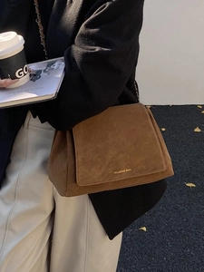 Brown suede shoulder bag with chain strap and gold logo shown in street style shot