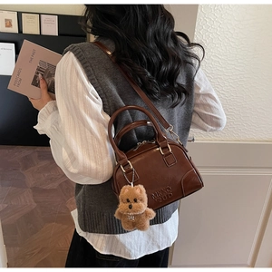 Detail of a brown polished leather Boston bag with teddy bear charm and letter embossing
