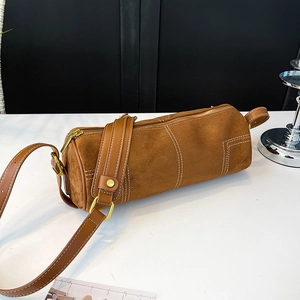 Close-up of brown frosted cylinder bag featuring white contrast stitching and gold hardware